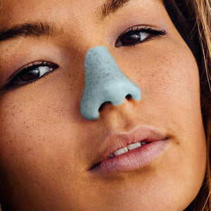 Women smirking into camera with blue NÖZ sunscreen on her nose.